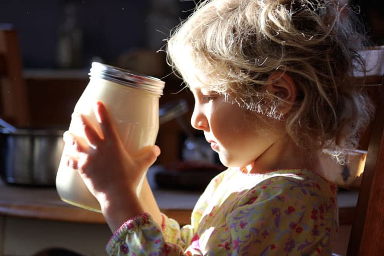 A child holding the jar with cream for butter.