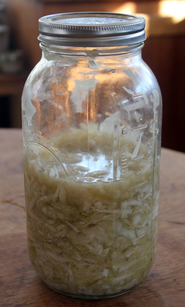 a half-full mason jar of homemade lacto-fermented sauerkraut on a wooden table