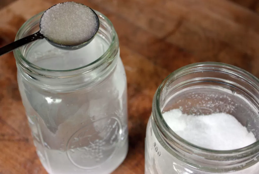 salt being added to a glass jar with water to make homemade brine