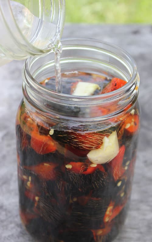 salt brine being poured on top of Fire-roasted jalapenos in a glass jar to make fermented hot sauce recipe