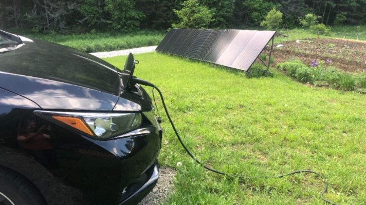 An electric vehicle charging with an off the grid solar panel array in the background.
